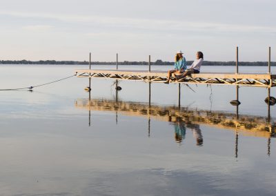 Two woman enjoying themselves sitting on the edge of a dock