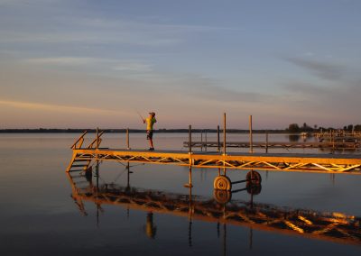 A young boy fishing off the dock at sunset