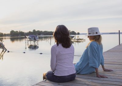 Two woman sitting on the edge of a dock over the water